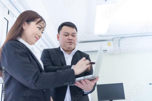 Two Asian business men and women looking at the laptop and talking about work projects at office. Asian business people, employee, and office staff. Concept