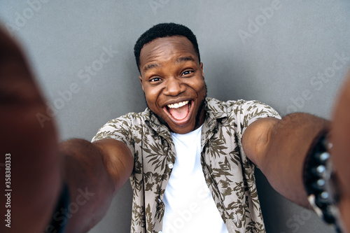 Phone selfie. Cheerful attractive afro american guy in a fun mood takes a selfie on his phone using the front camera