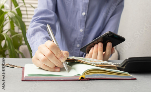 Young woman freelancer writing with pen ideas in notepad while using mobile phone. focus on woman s hand.