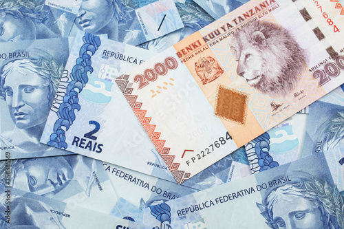 A close up image of a two thousand Tanzanian shilling bank note on a background of Brazilian two reais bank notes