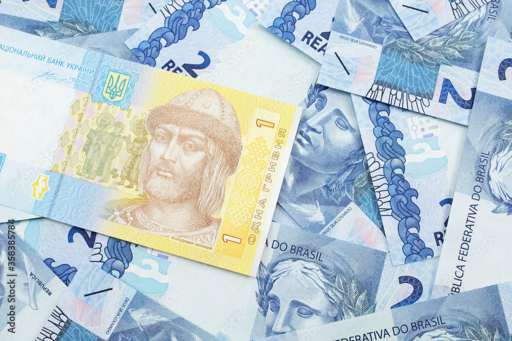A blue and yellow one Ukrainian hryvnia bank note on a bed of Brazilian two reais bank notes