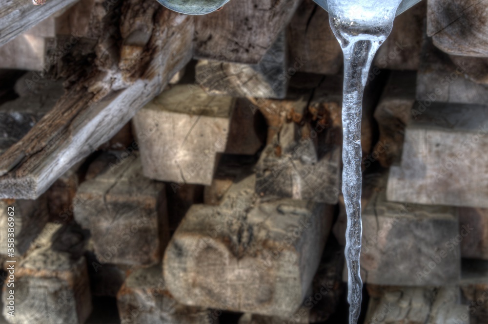 melting icicle hanging in front of wooden pole stack melting icicle hanging in front of wooden pole stack