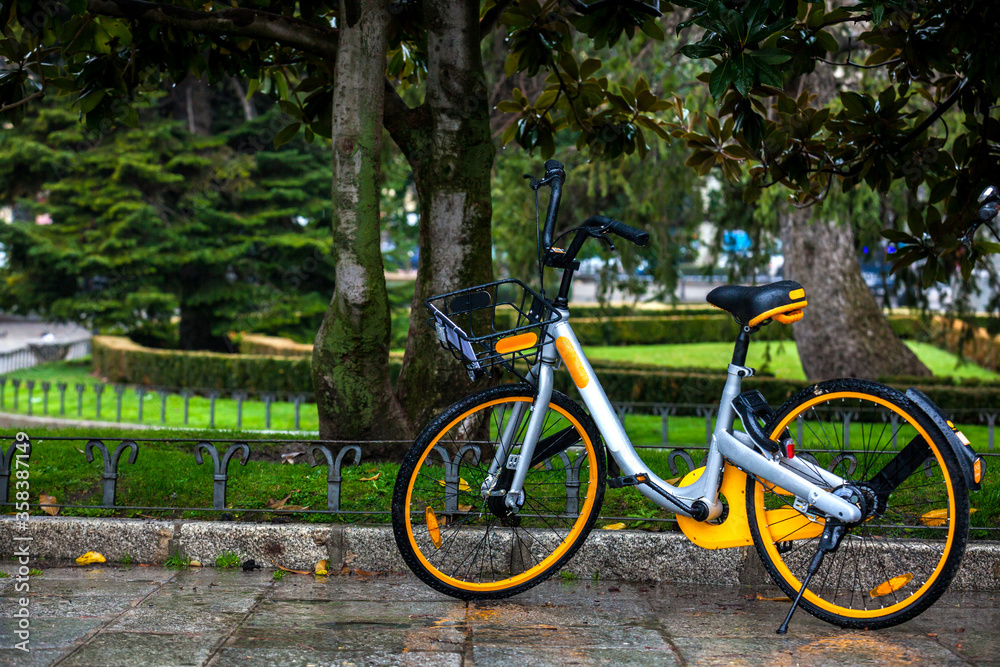Yellow rental public bike parked at the Paseo del Prado on a rainy day in Madrid