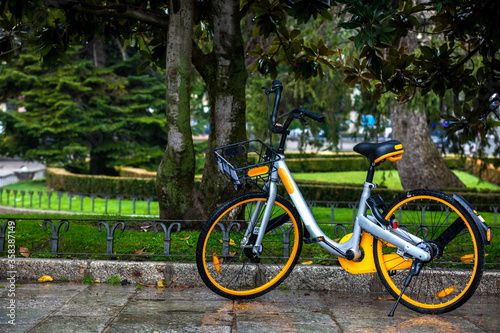 Yellow rental public bike parked at the Paseo del Prado on a rainy day in Madrid