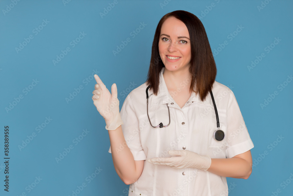 Happy female doctor in medical gloves with stethoscope pointing to copy space, advertise clinic for medical pharmacies, medicines on blue background Happy female doctor in medical gloves with stethoscope pointing to copy space, advertise clinic for medical pharmacies, medicines on blue background