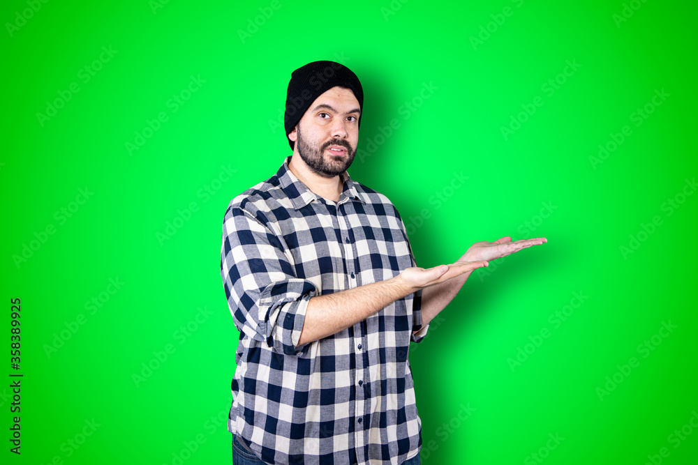 Fototapeta premium Young man pointing and looking at copy space. Handsome young businessman isolated on green background