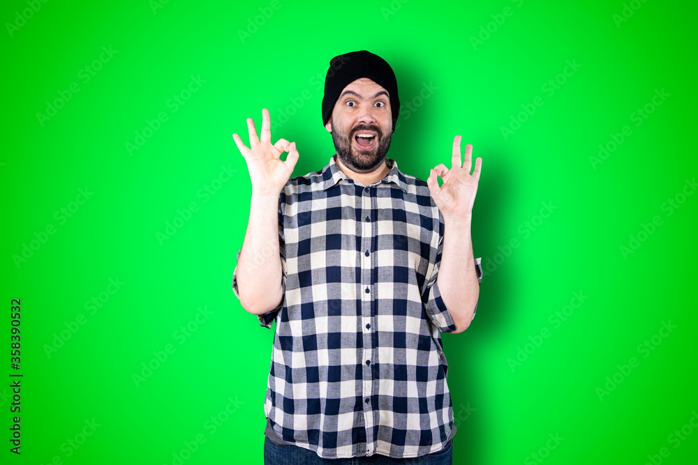 Naklejka premium Portrait of a cheerful young man showing okay and victory gesture isolated on the chroma background