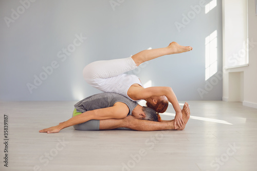 Yoga couple practice acro yoga on the floor in a studio class.