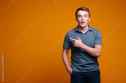 Red-haired guy with his fingers shows on an empty place to insert his text on an orange background. Advertising banner.