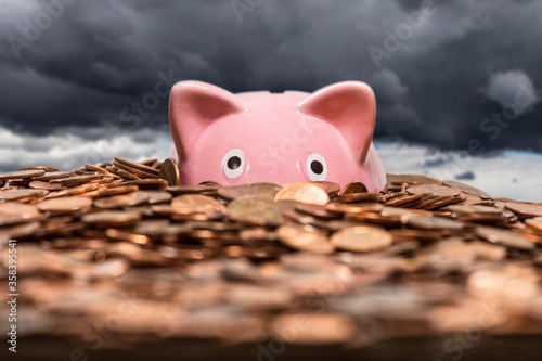 Pink piggy bank drowning in ocean of copper pennies with gathering storm clouds in background.