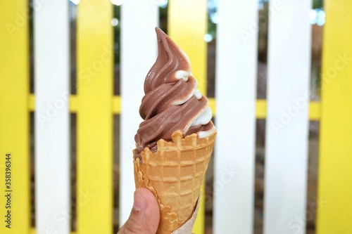 Two tone Ice cream conne with a female hand holding and blurred white yellow fence background