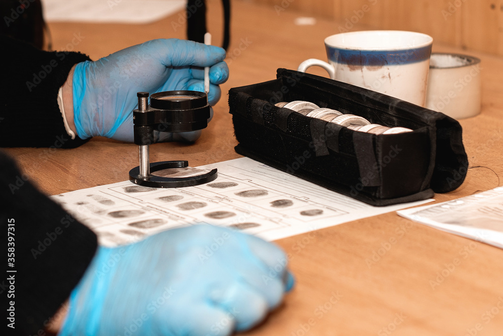 rubber-gloved detective takes fingerprints from surfaces at a crime scene. forensic expert with magnifier and investigation tools