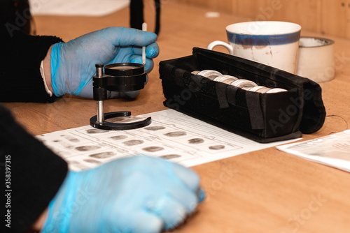 Obraz na płótnie rubber-gloved detective takes fingerprints from surfaces at a crime scene. forensic expert with magnifier and investigation tools w salonie