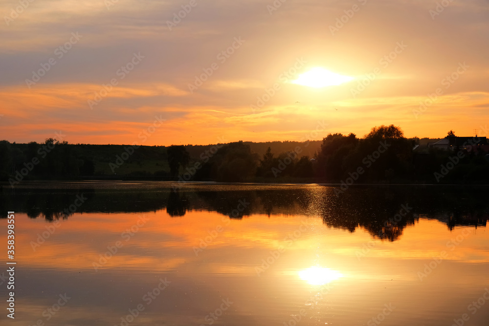 mellow sunset on countryside landscape with rural scenery reflection in pond water. Natural color of summer evening nature. Wide view