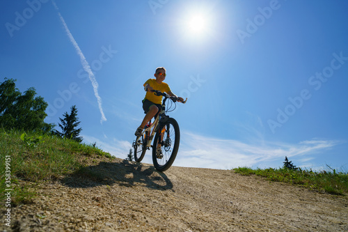 The boy rides from the mountain on a bicycle on a background of blue sky
