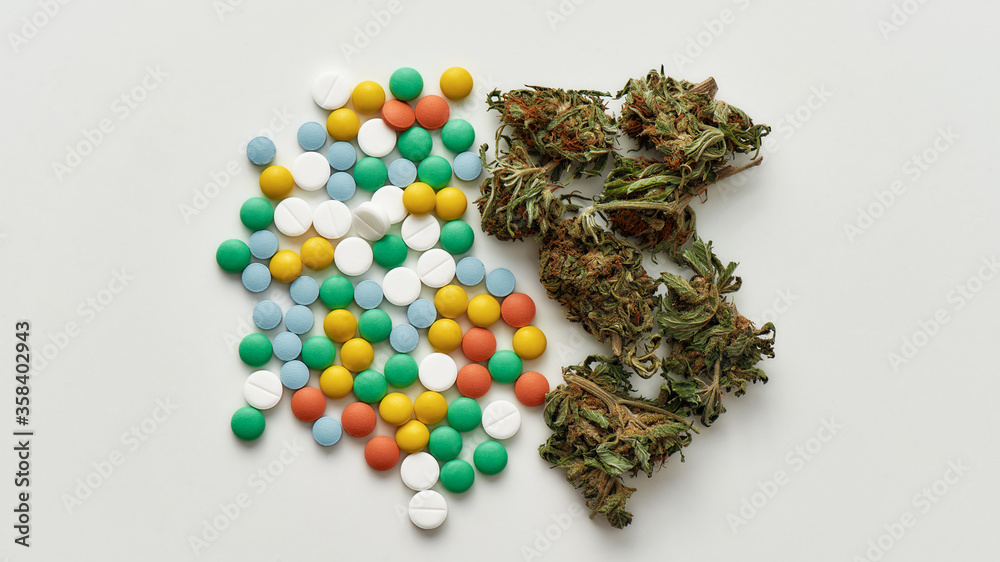 Top view of medical marijuana buds and colorful pills over white background. Concept of herbal, alternative medicine Top view of medical marijuana buds and colorful pills over white background. Concept of herbal, alternative medicine