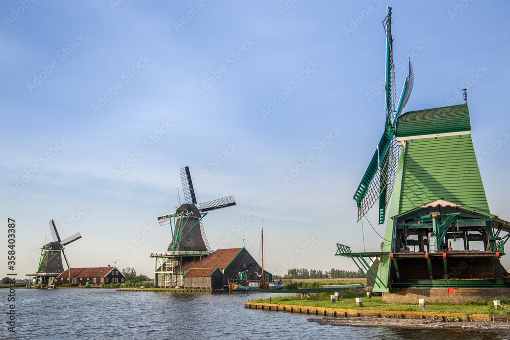 Three Dutch windmills near a lake on a summer's evening with blue skies 