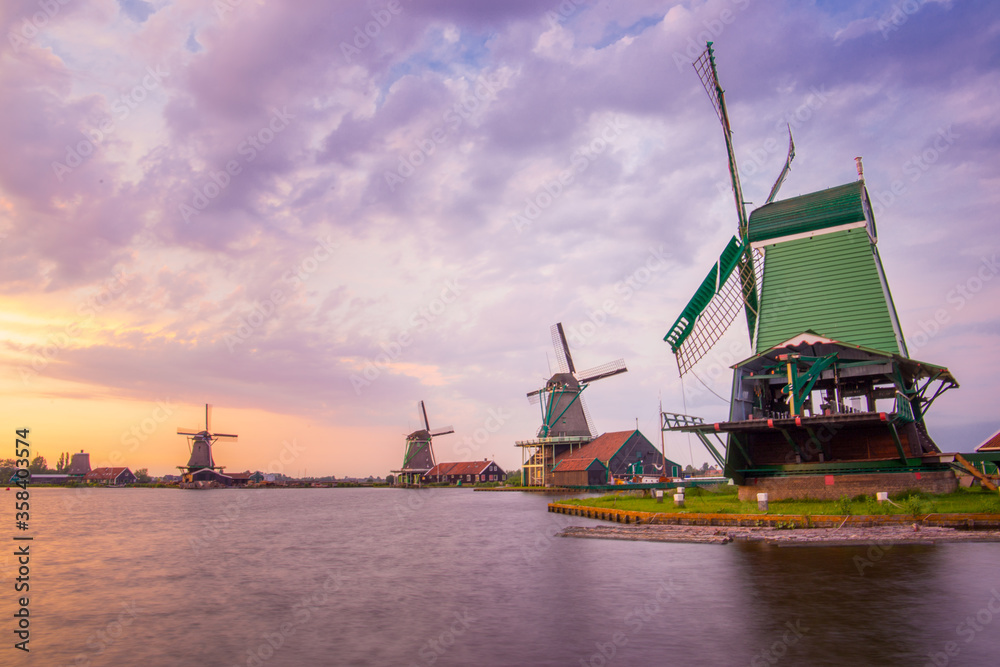 Three Dutch windmills near a lake on a summer's evening with purple sunset skies 