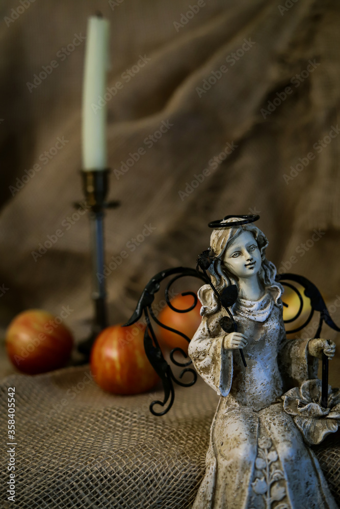 statuette of a sitting girl with wings on a background of red apples and candles in a candlestick close up