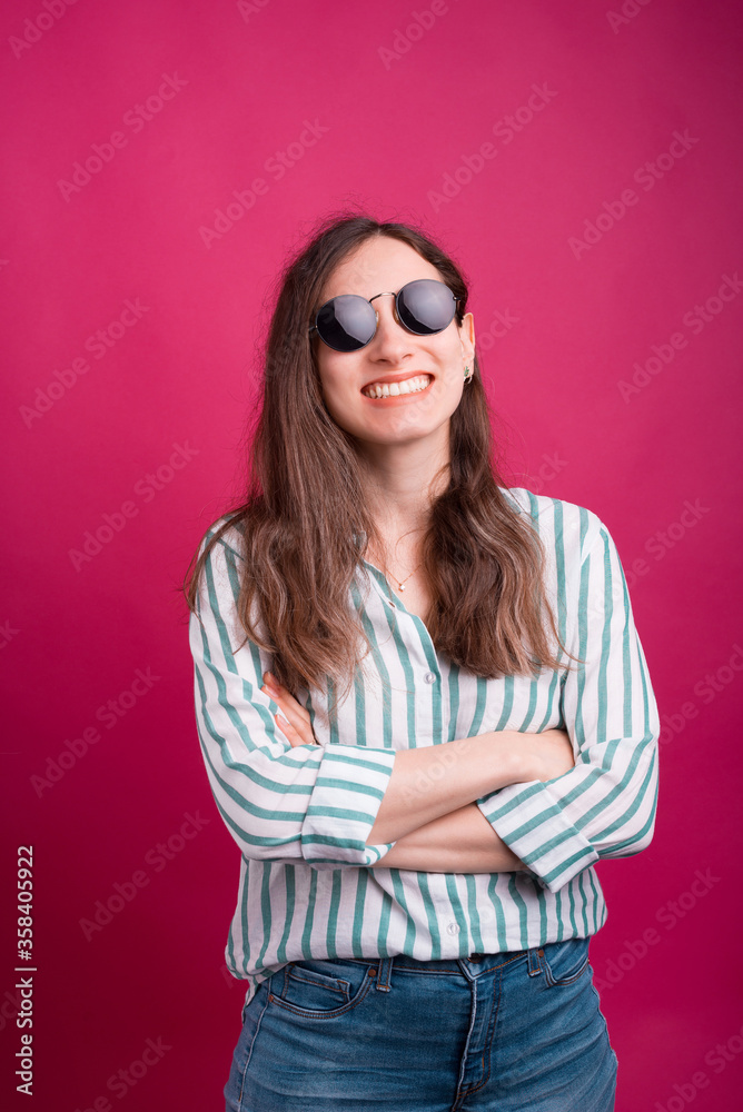Smiling girl with arms crossed is wearing sunglasses over pink background Smiling girl with arms crossed is wearing sunglasses over pink background