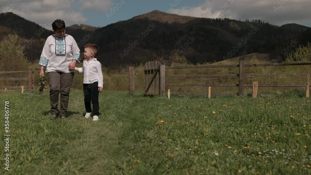 Grandchild supports grandma when walking, a grandson goes through nature with his grandparent, listening to their stories, outdoor over mountain on background, generarion family. Bright sunny day Grandchild supports grandma when walking, a grandson goes through nature with his grandparent, listening to their stories, outdoor over mountain on background, generarion family. Bright sunny day