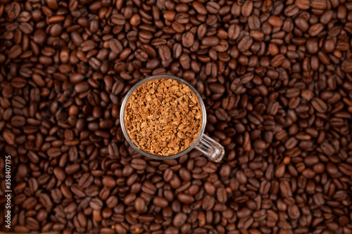 Instant, freeze-dried or granulated coffee in a transparent cup on the background of roasted coffee beans. Used to make a cold Dalgon coffee drink. Selective focus. Top view