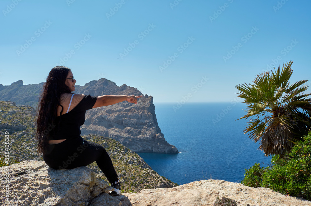 Latin girl, happy, with long brown hair on a spring day, Making indications, in Cape de Formentor, Mallorca, Balearic islands, Spain,