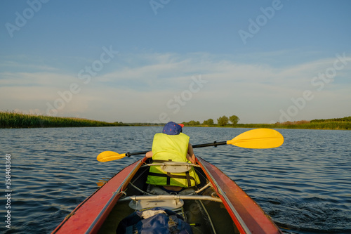 A little boy kayaks on the river in the summer and rowing an oar. The boy is floating in a boat on the river.