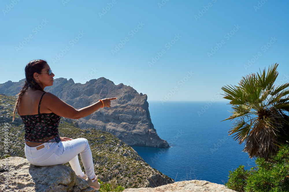 happy latin woman with long brown hair on a spring day, making indications, in cape de formentor, Mallorca, Balearic islands, Spain,