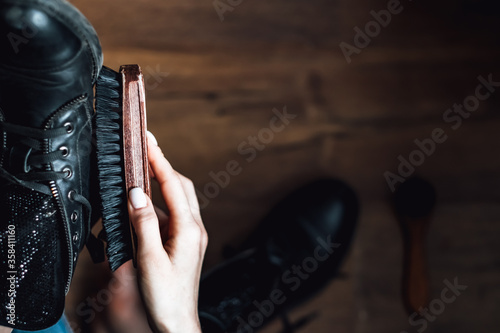 Woman brushing black leather shoes on wooden background. close up photo