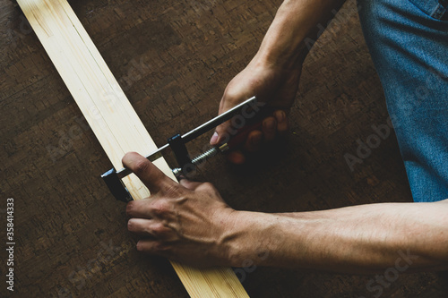 Men's hands fasten the clamp to the wooden rails, making a measurement before cutting. Repair concept