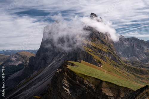 Dolomites Alps. Ortisei. Italy. Landscape of mountains Sass Rigais, Furcheta, Fermeda peaks in white cloud with cliffs & green slope meadows from the top of mountain Seceda on blue sky background photo