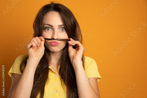 funny young woman who makes a mustache with a lock of her hair on an orange background