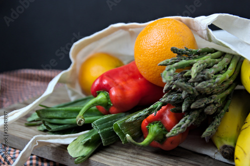 Cloth bag with usual fruits and vegetables on a table and dark background