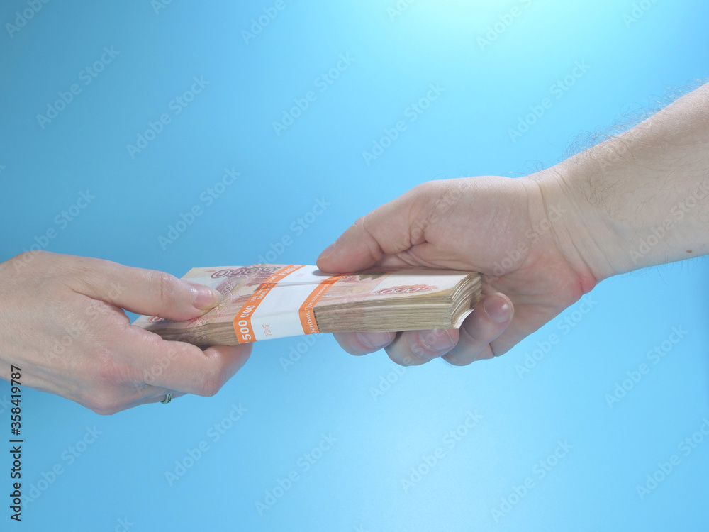 Obraz premium Woman's hand gives stack of cash to man's hand on blue background