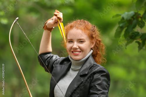 Sporty young woman practicing archery outdoors photo