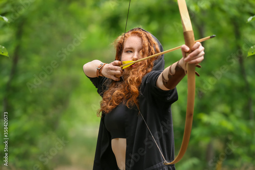 Sporty young woman practicing archery outdoors