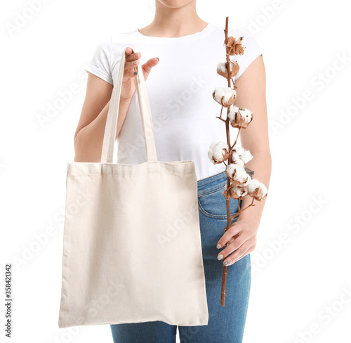 Beautiful young woman with cotton flowers and shopping bag on white background