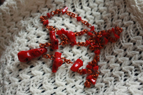 Red beads made of natural coral and copper wire on a white knitted background.