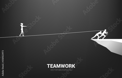 Silhouette of businesswoman walking on rope walk way pulled by team.Concept for teamwork and team support..