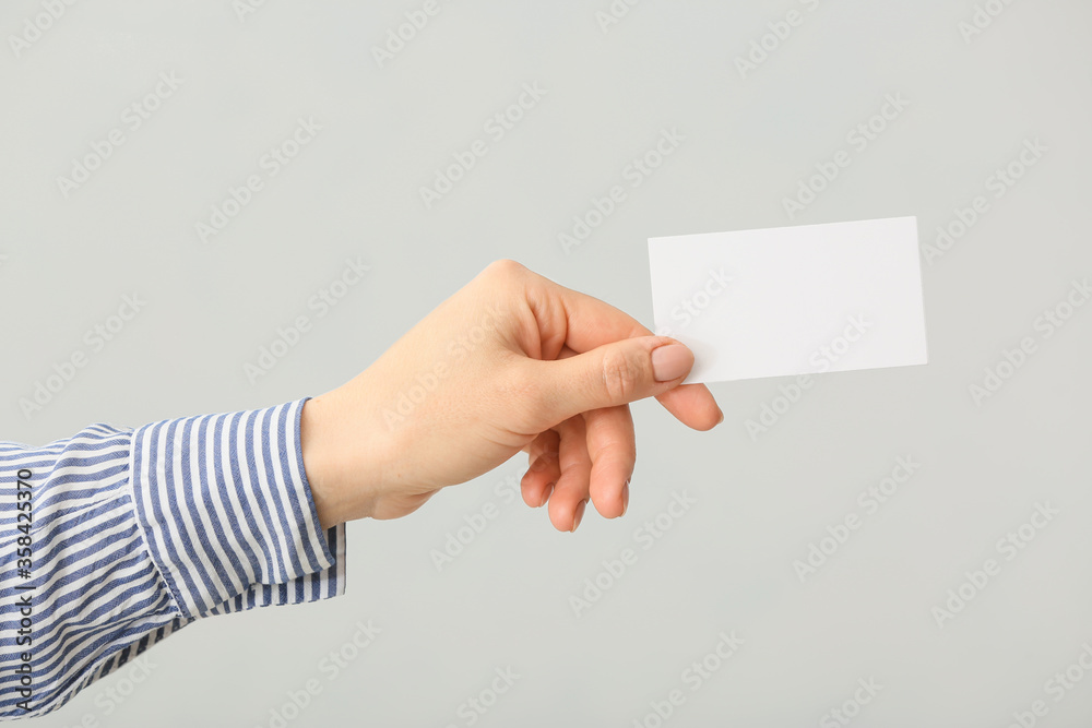 Female hand with blank business card on light background Female hand with blank business card on light background