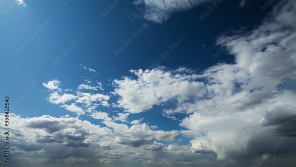 Beautiful timelapse of white fluffy clouds moving softly across blue sky in bright sunshine with dense overcast on the background. 
