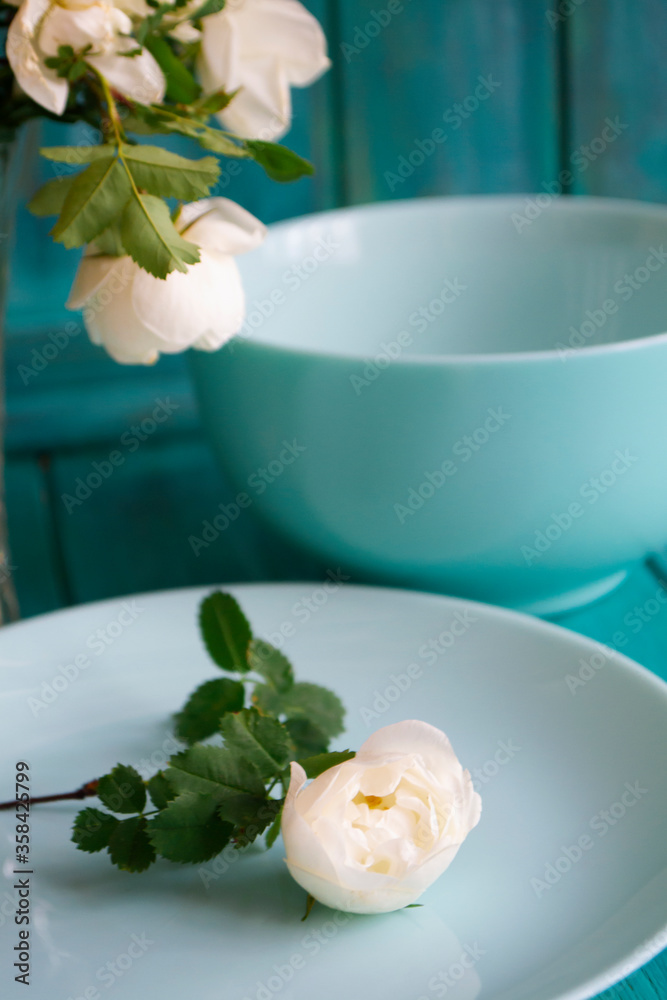 Romantic table setting with bouquet of roses, dishware, on holiday teal table. Romantic and wedding anniversary.