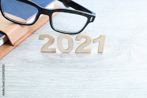 Block letters on 2021 and eyeglasses and a notebook at the back on wooden table 