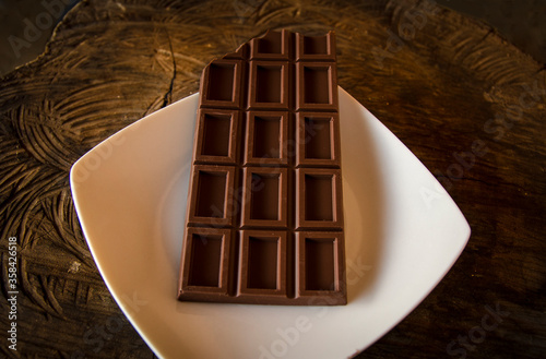 Konstfotografi Dark chocolate bar over white dish and wood texture