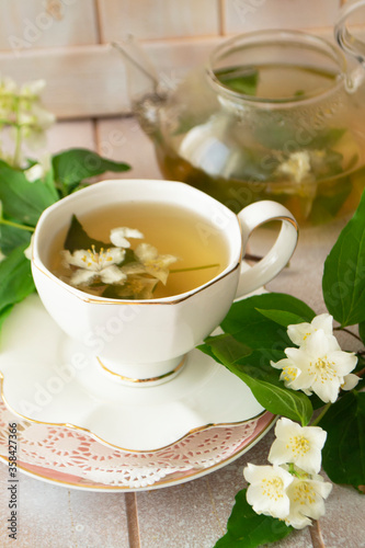 Jasmine tea with jasmine flowers on white wooden table background. Cup of hot green tea with jasmine flavor, fresh jasmine flowers. Concept of freshly drink.