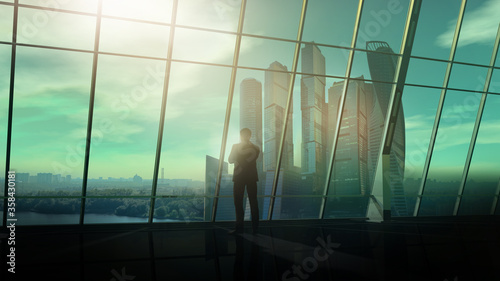 Against the large office window, a man stands and looks into the distance.