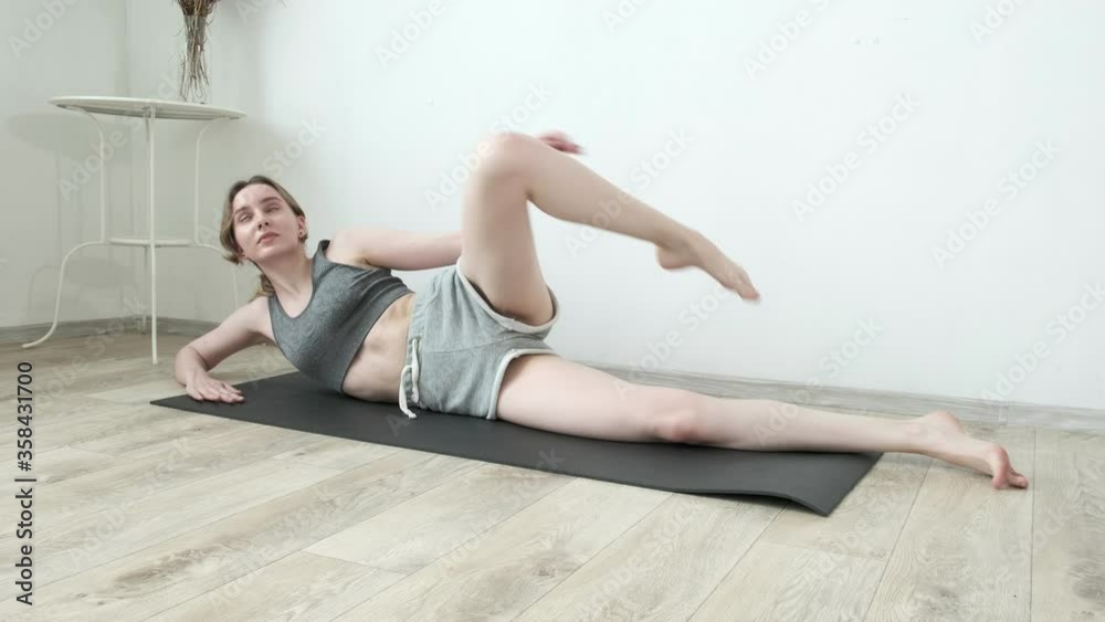 young slim pretty girl in sportswear practicing yoga at home. fit flexible female in shorts raises leg up lying on mat. fitness training, sport, yoga, healthy lifestyle, stretching, pilates, workout young slim pretty girl in sportswear practicing yoga at home. fit flexible female in shorts raises leg up lying on mat. fitness training, sport, yoga, healthy lifestyle, stretching, pilates, workout