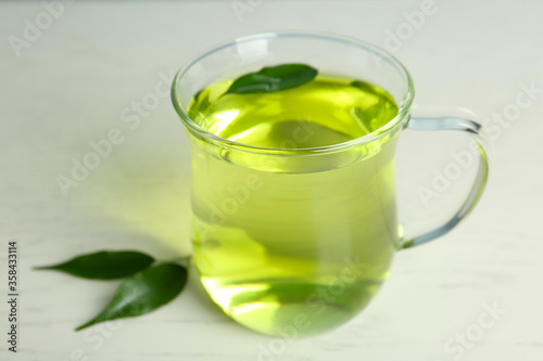 Cup of aromatic green tea and leaves on light wooden table
