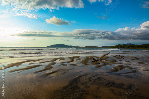 Fototapeta Naklejka Na Ścianę i Meble -  Setting sun reflecting in the rolling sand and glass waters of Tamarindo beach, Costa Rica
